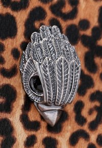 Broche métallique en bronze en forme de feuille, présentant des textures détaillées et une pierre noire incrustée, sur un fond en imprimé léopard.