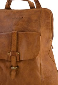 Sac à dos en cuir tan avec une finition texturée, une poche avant avec fermeture à boucle et des détails de couture visibles.