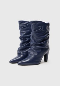 Botine din piele bleumarin cu un design lejer, vârf ascuțit și toc de 7 cm înălțime. Textură netedă cu o strălucire subtilă.