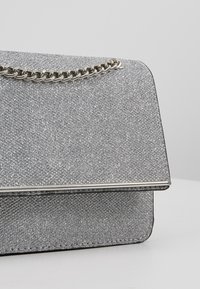 Borsa da sera argentata con glitter, caratterizzata da una superficie testurizzata, una tracolla in catena argentata e una chiusura a scatto strutturata con finitura metallica.