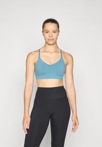 Világoskék sportmelltartó V-nyakkal és vékony pántokkal, finom mintás textúrával. Magas derekú fekete leggings-szel párosítva.