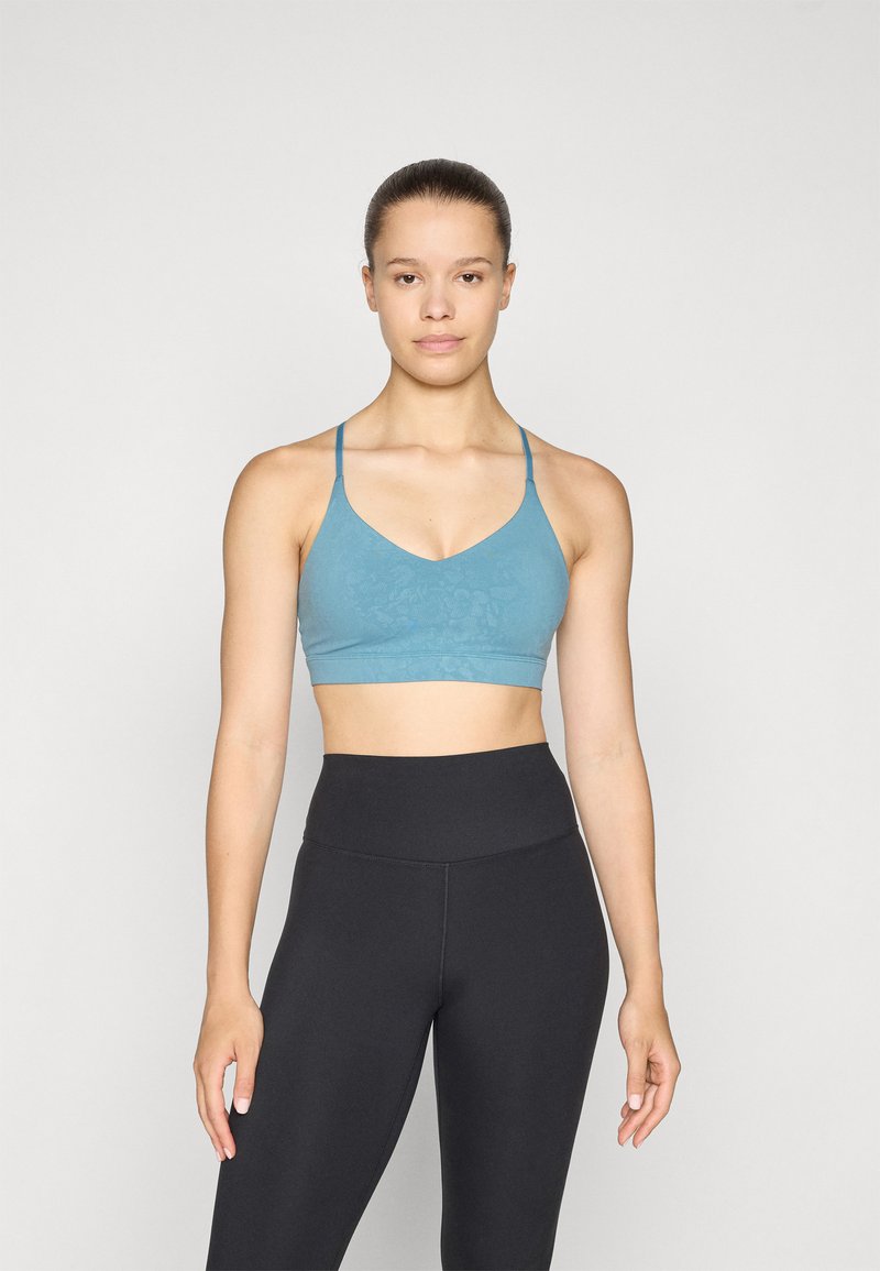 Világoskék sportmelltartó V-nyakkal és vékony pántokkal, finom mintás textúrával. Magas derekú fekete leggings-szel párosítva.