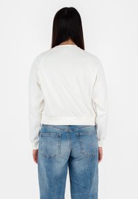 Felpa corta bianca con polsini e orlo a costine, caratterizzata da una texture liscia e maniche raglan, abbinata a jeans baggy azzurri sbiaditi.