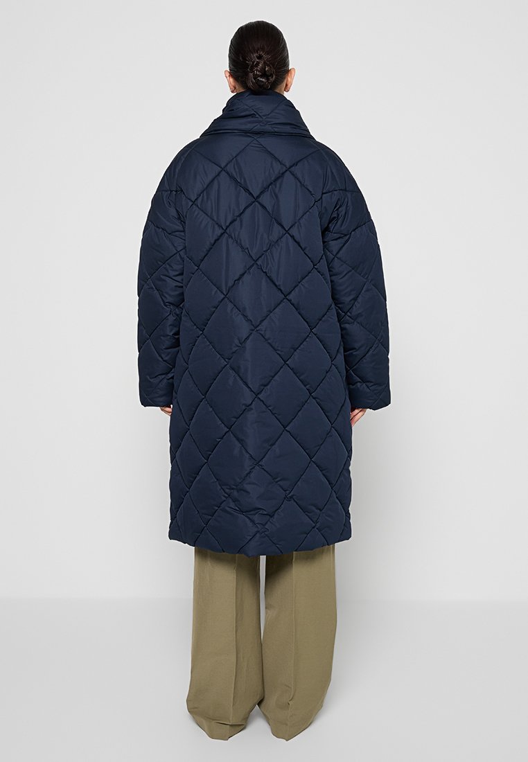 Granatowy pikowany płaszcz puchowy z wysokim kołnierzem i wzorem w diamenty, z długimi rękawami i długością do kolan.