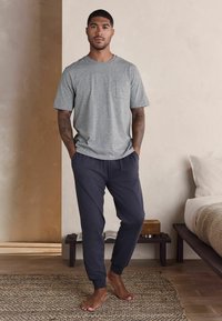 Grå kortærmet t-shirt med en lomme, parret med mørkeblå joggerbukser. Blød bomulds-blanding, afslappet pasform, elastiske manchetter ved anklerne.