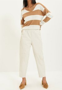 Bruine en witte gestreepte losse trui, crèmekleurige tapered broek met zijnaaddetails en tan kleurige hakken met een strikaccent.