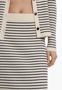 Set composto da cardigan e gonna a maglia in crema con righe orizzontali blu navy, caratterizzato da chiusura a bottoni e polsini e vita a costine.
