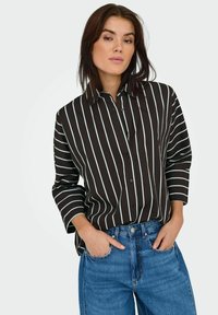 Zwart-witte gestreepte blouse met een kraag, voorzien van losse mouwen, gedragen met blauwe high-waisted spijkerbroek.