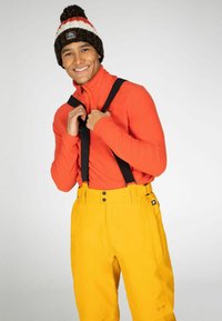 Felgekleurde oranje fleece zip-up trui met zwarte bretels, gecombineerd met gele waterdichte broek met knoopsluitingen en een logo aan de zijkant.