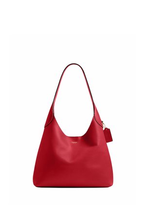 Sac à bandoulière en cuir rouge avec une lanière simple et une petite étiquette suspendue, texture lisse et petit logo doré au centre devant.