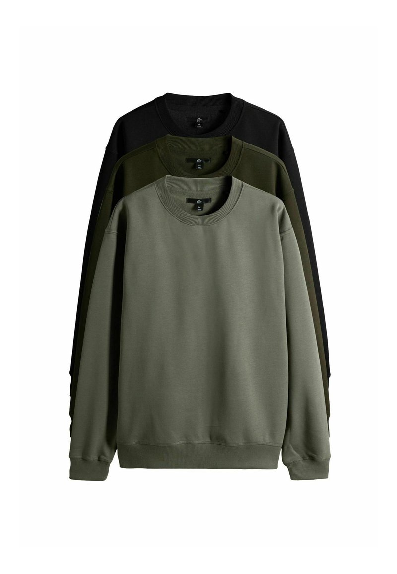 Tričko s okrúhlym výstrihom v troch farbách, usporiadané vertikálne. Farby sú tmavozelená, olivovo zelená a čierna. Vyrobené z hladkej, pevnej textílie s rebrovanými manžetami.