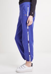 Paarse joggingbroek met elastische boorden, voorzien van zijstrepen in het wit met logo-accenten. Gemaakt van zachte stof met zakken.