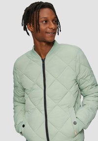 Gequiltede bomberjack in lichtgroen, met een zwarte rits, zijzakken, geribbelde manchetten en een opstaande kraag.