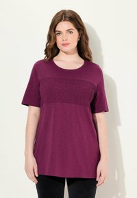 Camiseta de mujer en púrpura oscuro con mangas cortas y un detalle de fruncido texturizado en el pecho. Corte relajado, tela suave.