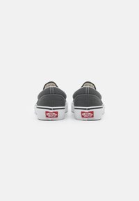 Ballerines en toile grise avec semelles en caoutchouc blanches, des coutures contrastantes et des détails de logo rouge sur le talon. Design arrondi et profil bas.