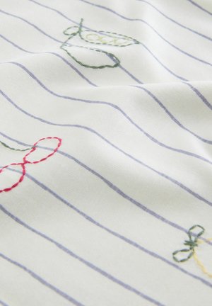 Tissu blanc à rayures bleues fines présentant des motifs brodés multicolores, y compris des feuilles vertes et des nœuds rouges, créant un aspect texturé.