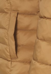 Brun dynejakke i stof med en glat, skinnende tekstur, vandrette quiltede sektioner og en skjult lomme på siden.