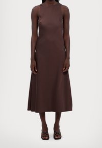 Braunes satinartiges, ärmelloses Kleid mit gerader Silhouette, knielangem Saum und subtiler Glanz. Tragen mit schwarzen Riemchensandalen.