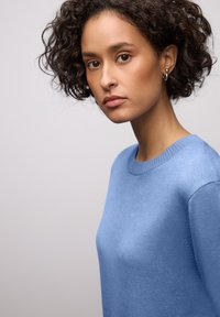 Pull bleu clair en maille avec un col rond et des détails côtelés. Le tissu semble doux et lisse, avec une texture et une structure subtiles.
