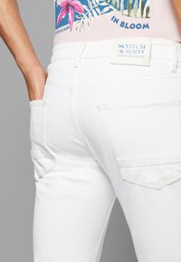 Hvide denim jeans med baglommer, en glat tekstur og et mærke tag mærket "Scotch & Soda Amsterdam."