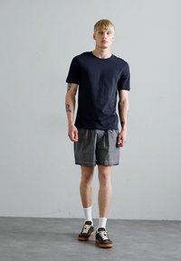 Marine bomull t-skjorte kombinert med grå shorts. Modellen har på seg brune joggesko med hvite snører og hvite ankelsokker. Enkelt design, avslappet passform.