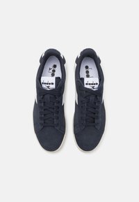 Adidași din velur bleumarin cu accente albe, vârf rotund, șnururi plata și detalii perforate. Logo pe limba și pe panoul lateral. Talpă din cauciuc netedă.