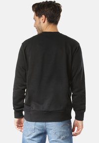 Felpa nera con scollo rotondo, polsini e orlo a costine, abbinata a jeans azzurri chiari. Texture liscia, design minimalista.