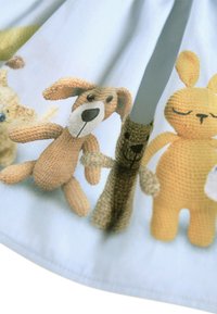 Kotni material z svetlo modro podlago in štirimi kvačkanimi igračami: psom, medvedkom, zajcem in rumeno živaljo, pri čemer ima vsaka od njih edinstveno teksturo.