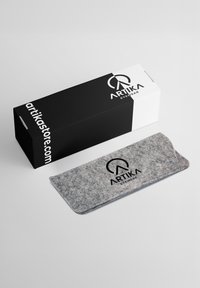 Custodia per occhiali in feltro grigia con bordi arrotondati, caratterizzata da un logo nero. Fornita con una scatola bianca e nera con marchio e sito web stampati.