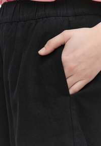 Svarta linnebyxor har en avslappnad passform med resårmidja och en hand placerad i en sidoficka för praktisk användning.
