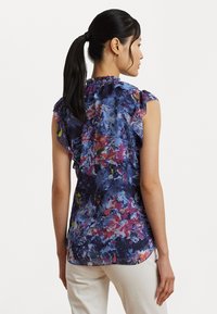 Short-sleeve blouse with a floral pattern in blue, pink, and green shades. Features ruffled shoulder details and a relaxed fit.