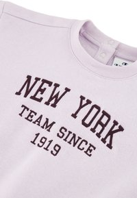 Sudadera de color púrpura claro con texto bordado en marrón oscuro: "NEW YORK TEAM SINCE 1919." Cuello redondo con cierres de presión en la parte posterior.