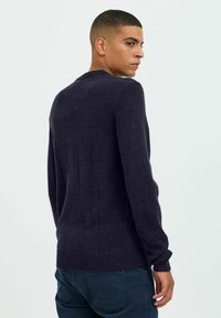 Pull en maille bleu marine foncé à manches longues et col rond, avec un ourlet et des poignets côtelés, texture lisse sans motifs.