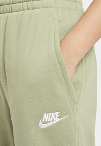 Olíva zöld Nike melegítő nadrágok puha tapintásúak, elasztikus derékpánttal és oldalsó zsebekkel rendelkeznek. A Nike logó fehér hímzéssel van ellátva.