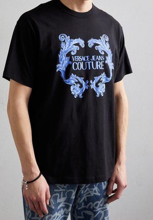 Sort bomulds t-shirt med blåt ornamentalt grafisk tekst, der læser "VERSACE JEANS COUTURE" på forsiden, korte ærmer og en afslappet pasform.