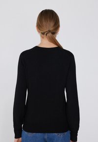 Schwarzer Pullover mit langen Ärmeln, Rundhalsausschnitt, geripptem Saum und strukturiertem Material. Die Rückansicht zeigt eine glatte Oberfläche ohne Verzierungen.