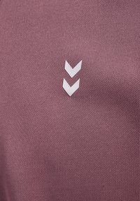 Le tissu du maillot violet présente une surface texturée avec deux logos en chevron blancs positionnés au centre.
