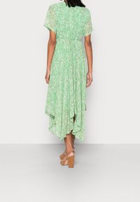 Grön blommig klänning med avslappnad passform, korta ärmar och lager-på-lager nederkant, med insydd midja och lättviktsmaterial. Bruna plattformssandaletter.