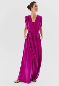 Dlouhé, splývavé šaty magentové barvy s volným střihem, širokým výstřihem a bočními kapsami. Vyrobené z měkké látky, s detailem zavazovacího pasu.