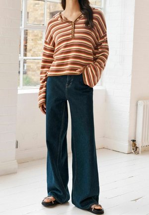 Gestreifter Pullover in warmen Tönen mit V-Ausschnitt und Knopfleiste; kombiniert mit weit geschnittenen, dunklen Jeans und schwarzen Riemchensandalen.