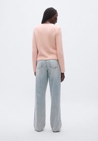 Texturált rózsaszín pulóver hosszú ujjakkal, kerek nyakkivágással; világoskék, bőszárú farmerral párosítva. Sima anyag finom mintázati részlettel.