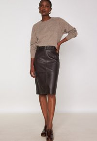 Jupe crayon en cuir marron avec une taille ceinturée, longueur genou, présentant des coutures et une texture lisse. Associée à un pull en maille beige.