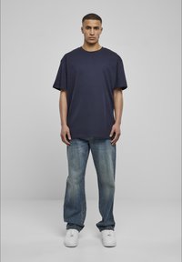 Tricou din bumbac de culoare bleumarin, cu mâneci scurte, asociat cu blugi drepti de culoare albastru deschis, ușor decolorati. Tenisi albi completează ținuta.