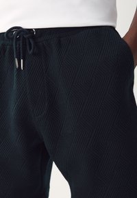 Dark blue joggers featuring a textured geometric pattern, elastic waistband with drawstring, and side pockets.