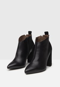 Bottes noires en cuir à cheville avec des orteils pointus, fermeture éclair sur le côté et talons blocs texturés noirs. Fini lisse avec doublure intérieure marron.