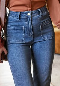 Jeans in denim a vita alta di blu medio, con due ampie tasche frontali, chiusura con bottone e gamba dritta con texture sottile.