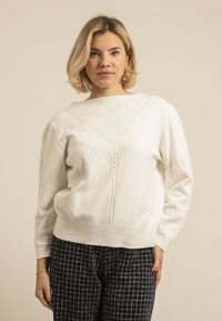 Pull en tricot blanc avec un motif côtelé au niveau de l'encolure et des épaules. Présente une taille ajustée et des manches longues.