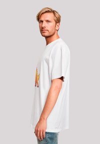 White cotton t-shirt featuring a colorful dinosaur graphic, short sleeves, and a relaxed fit. Model posed in profile against a neutral background.