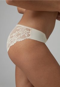 Beige kanten ondergoed met een zachte, gladde voorkant en ingewikkelde bloemenkantdetails aan de achterkant, met een gegolfde rand langs de tailleband.