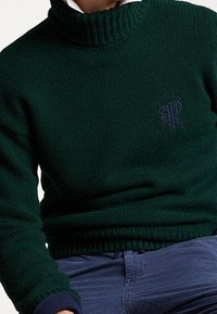 Vihreä neulepaita, jossa on korkea ribbireuna ja logo. Muotoillut hihansuut ja helma. Sileä pinta, joka korostaa lämp�öä ja mukavuutta.